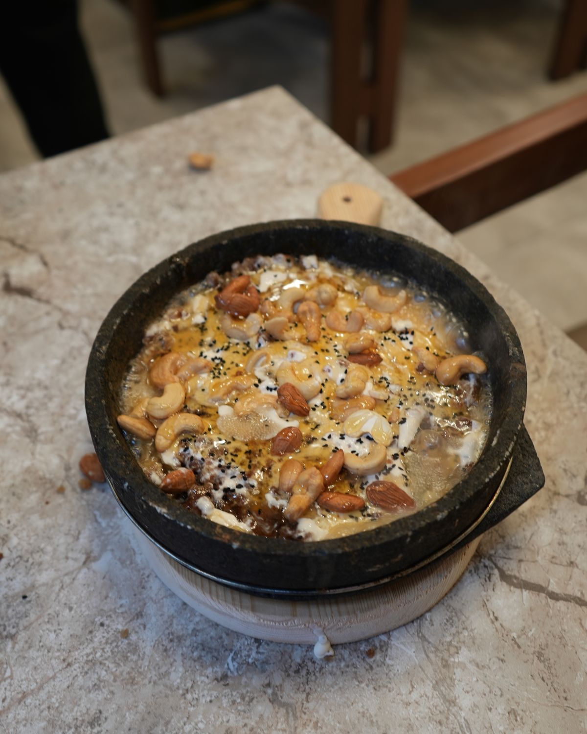 A warm Yemeni dish in a stone bowl, topped with almonds, cashews and honey