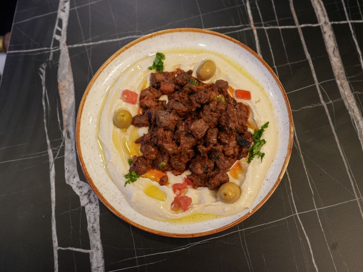 Hummus topped with spiced meat, olives and peppers