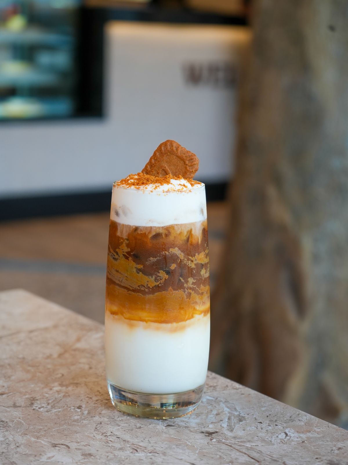 A layered iced latte in a tall glass, finished with a biscuit