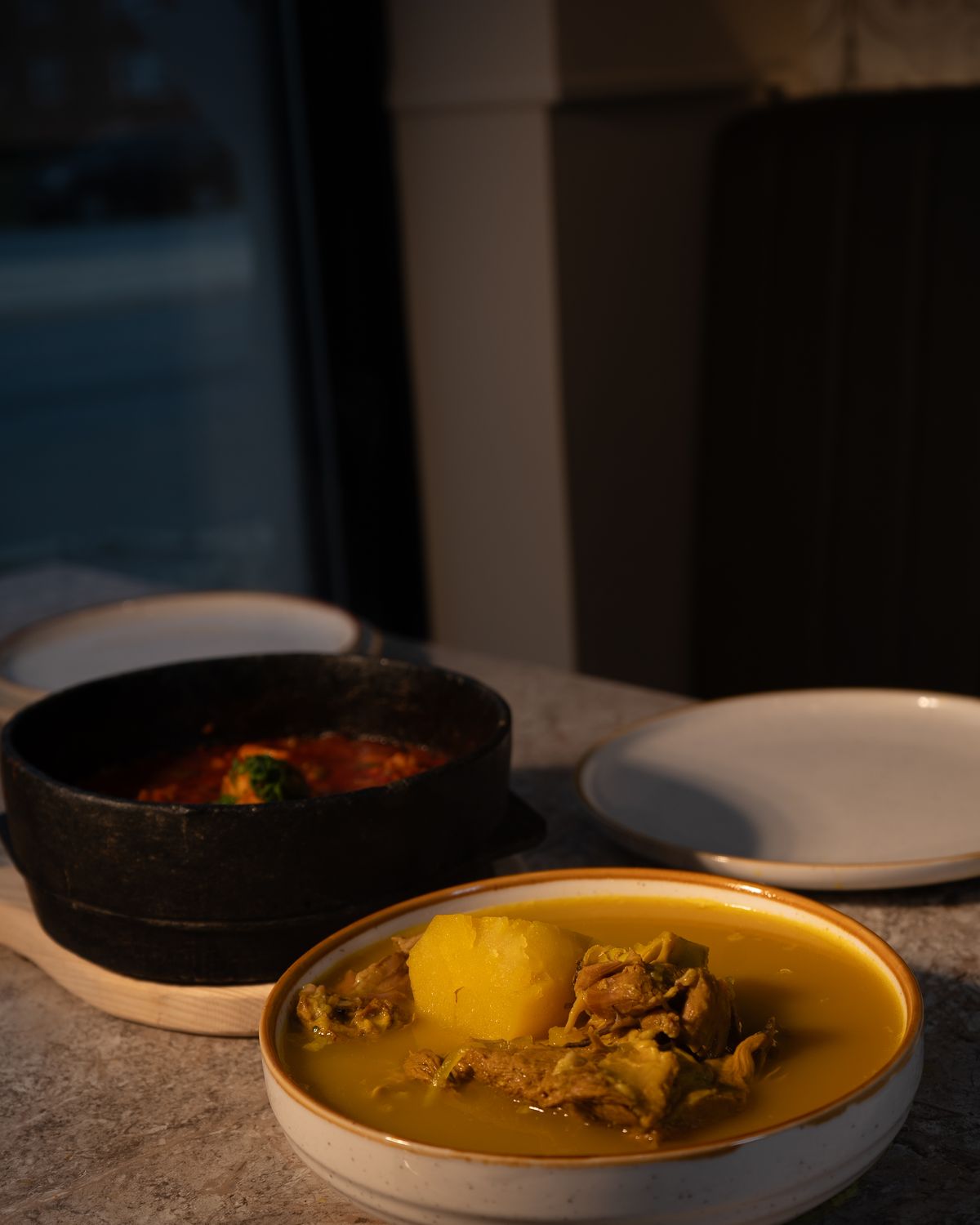 A stone pot of stew beside a bowl of marag broth